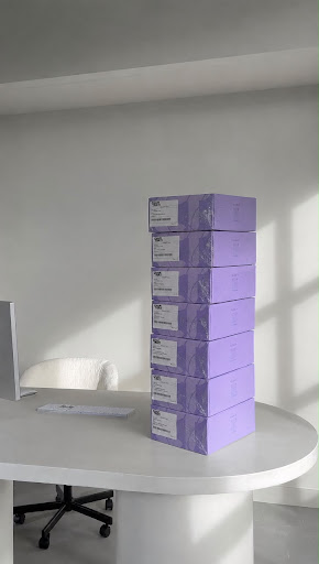 Pila de cajas de envío violetas de Chapitrati sobre escritorio blanco minimalista